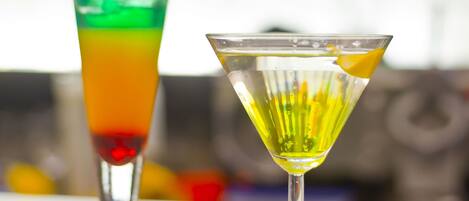 Two cocktails on a bar counter with a blurred background of bottles.