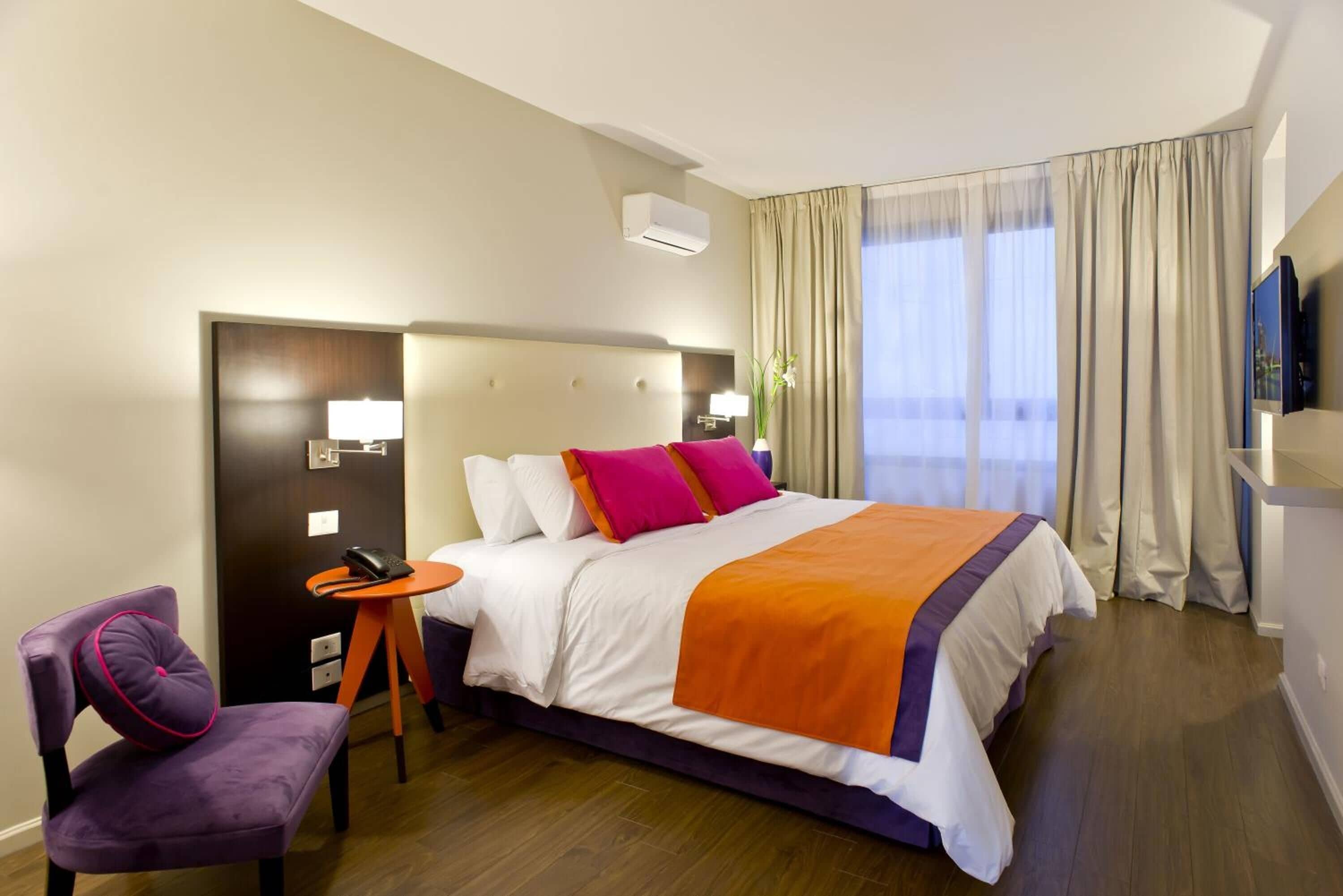 Een hotelkamer met een bed, een stoel, een tafeltje, een televisie en een raam met gordijnen.