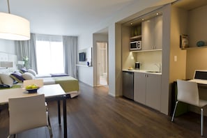 Quarto de hotel moderno com área de jantar, cozinha compacta e cama com vista.
