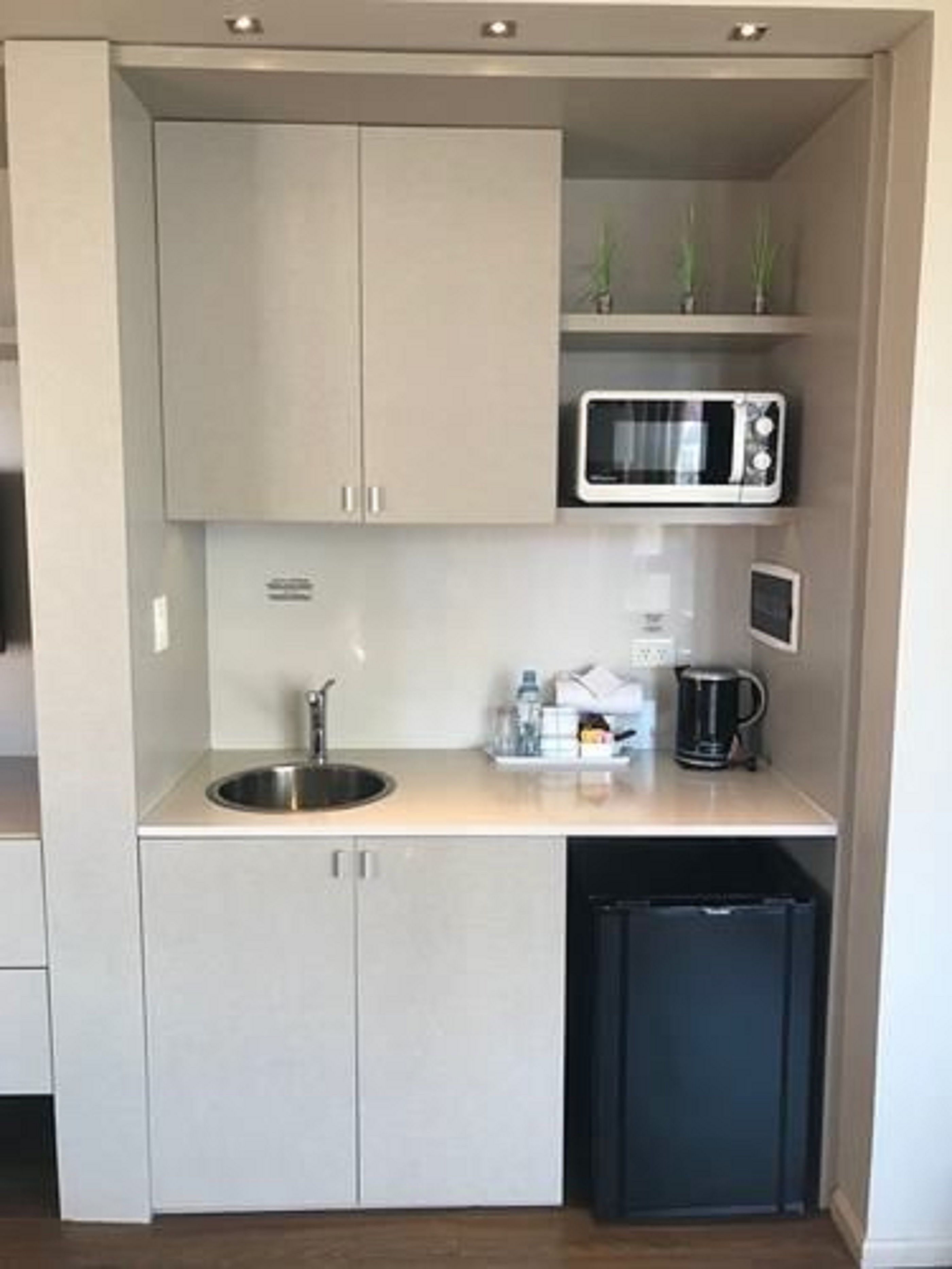 Una kitchenette compacta con pileta, microondas y heladera pequeña.