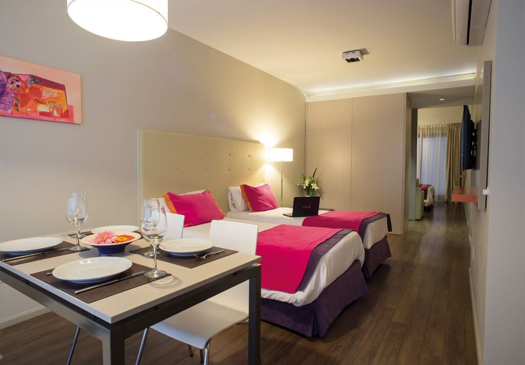A hotel room with two beds, a dining table with plates and glasses, a laptop, and a painting on the wall.