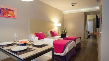 Habitación de hotel con dos camas, una mesa de comedor con platos y vasos, una computadora portátil y un cuadro en la pared.