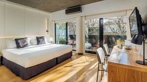 Un dormitorio moderno con una cama grande, suelo de madera, un escritorio con silla y vistas a través de un ventanal.