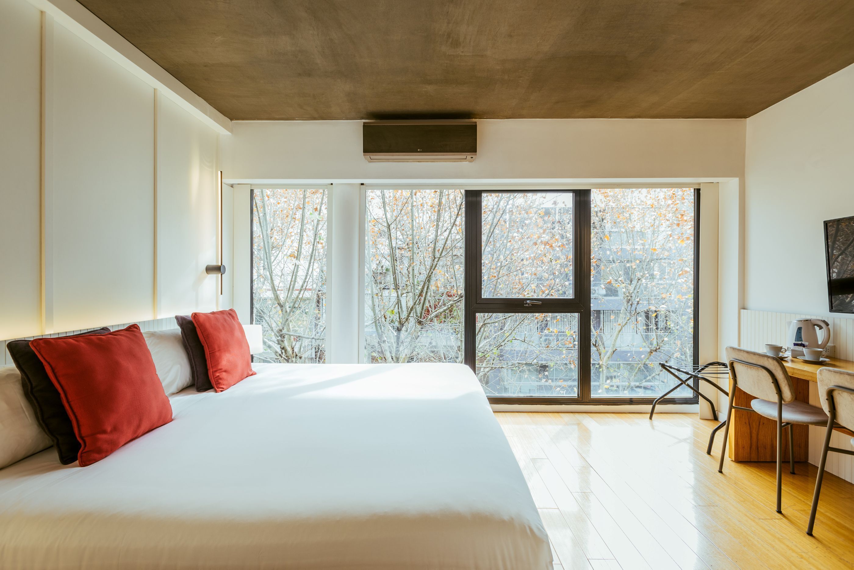 Une chambre d’hôtel moderne, dotée d’un grand lit, d’un bureau et offrant une vue sur la ville grâce à de grandes fenêtres.