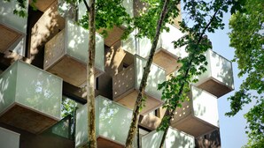 Un edificio moderno con varios balcones y un árbol en primer plano.