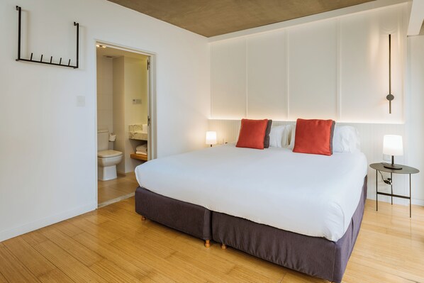 A modern bedroom with a large bed, wooden flooring, and a walk-in closet.