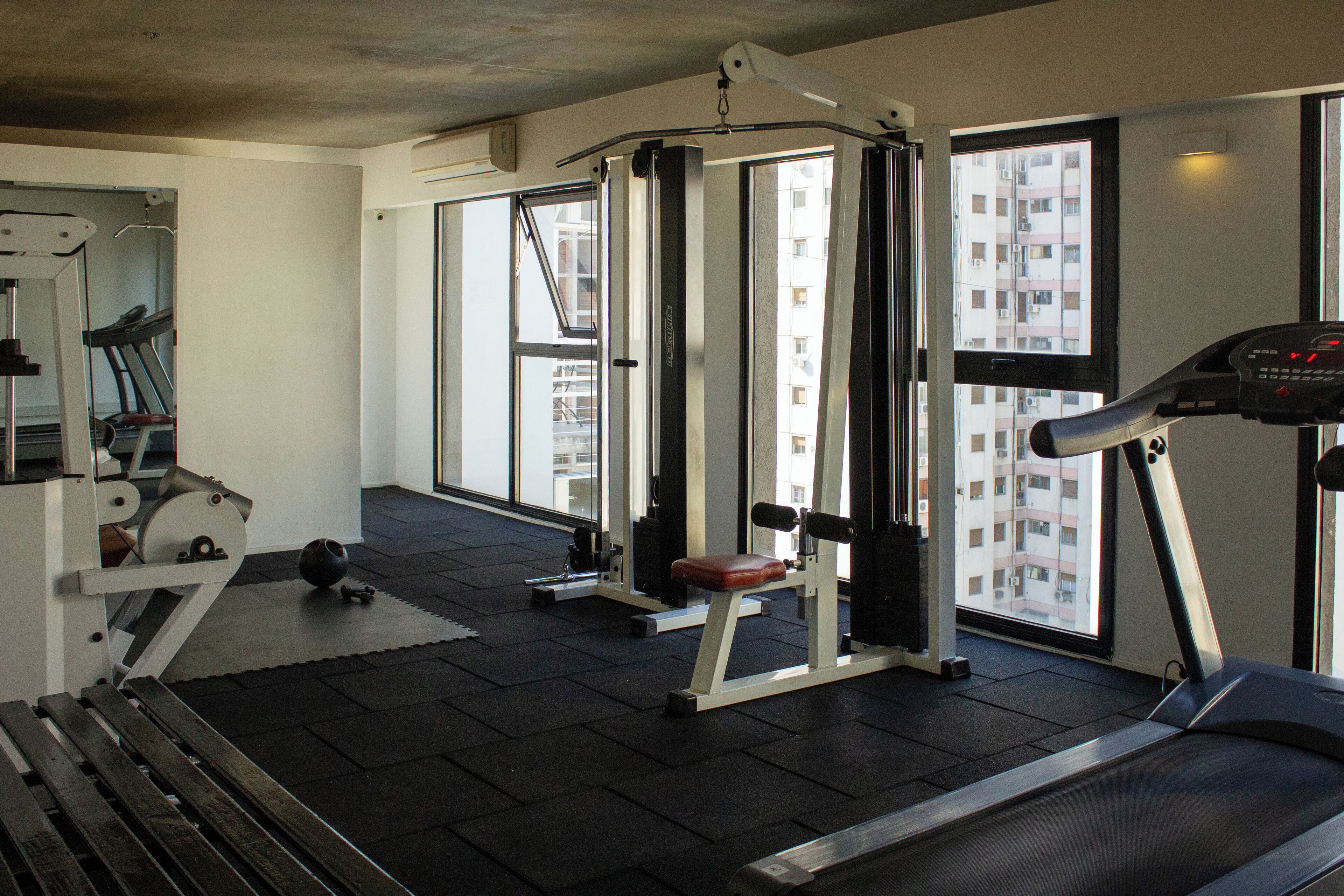 Uma academia com esteira, aparelho de musculação e colchonetes de exercício.