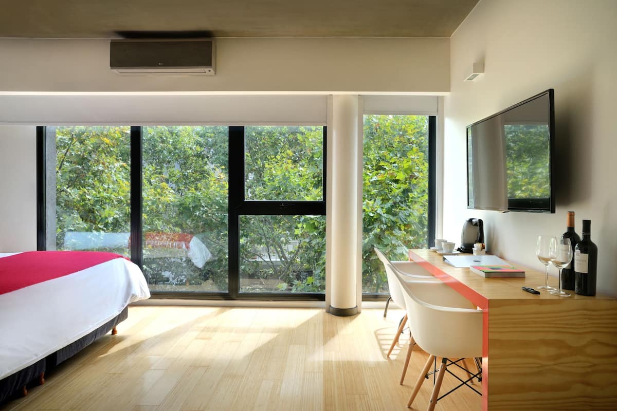 A modern hotel room with a bed, desk, chair, large windows, and a flat-screen TV.