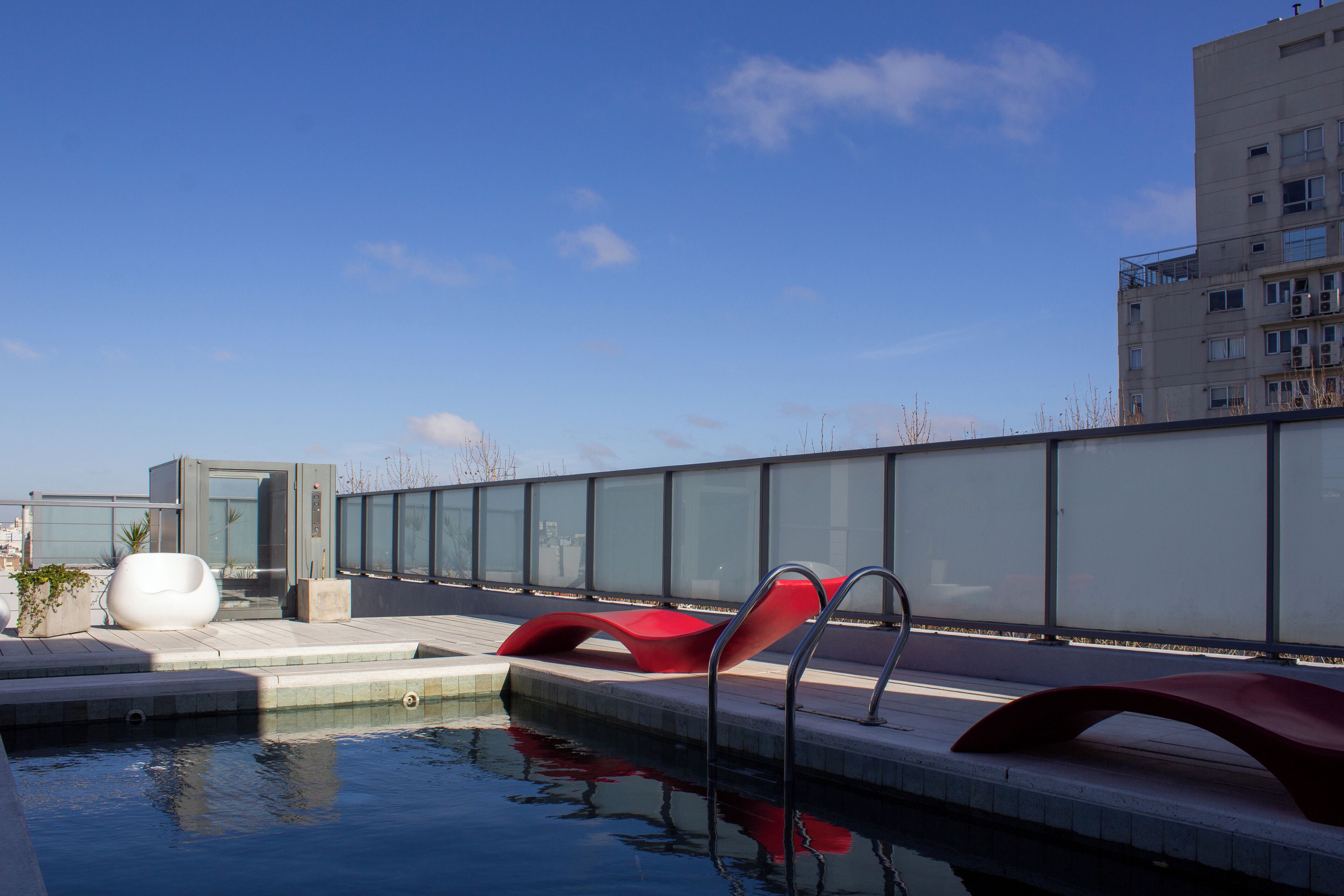 Un área de piscina en la azotea con mobiliario moderno y una barandilla de cristal.