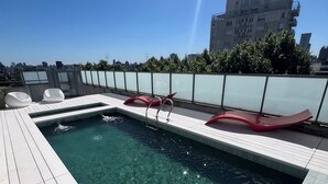 Una piscina en la azotea con agua cristalina, barandilla de vidrio y vista panorámica de la ciudad.