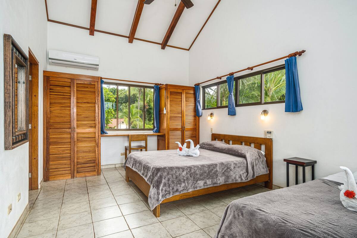 Un dormitorio con dos camas, cabeceros de madera, un escritorio y una ventana con cortinas azules.