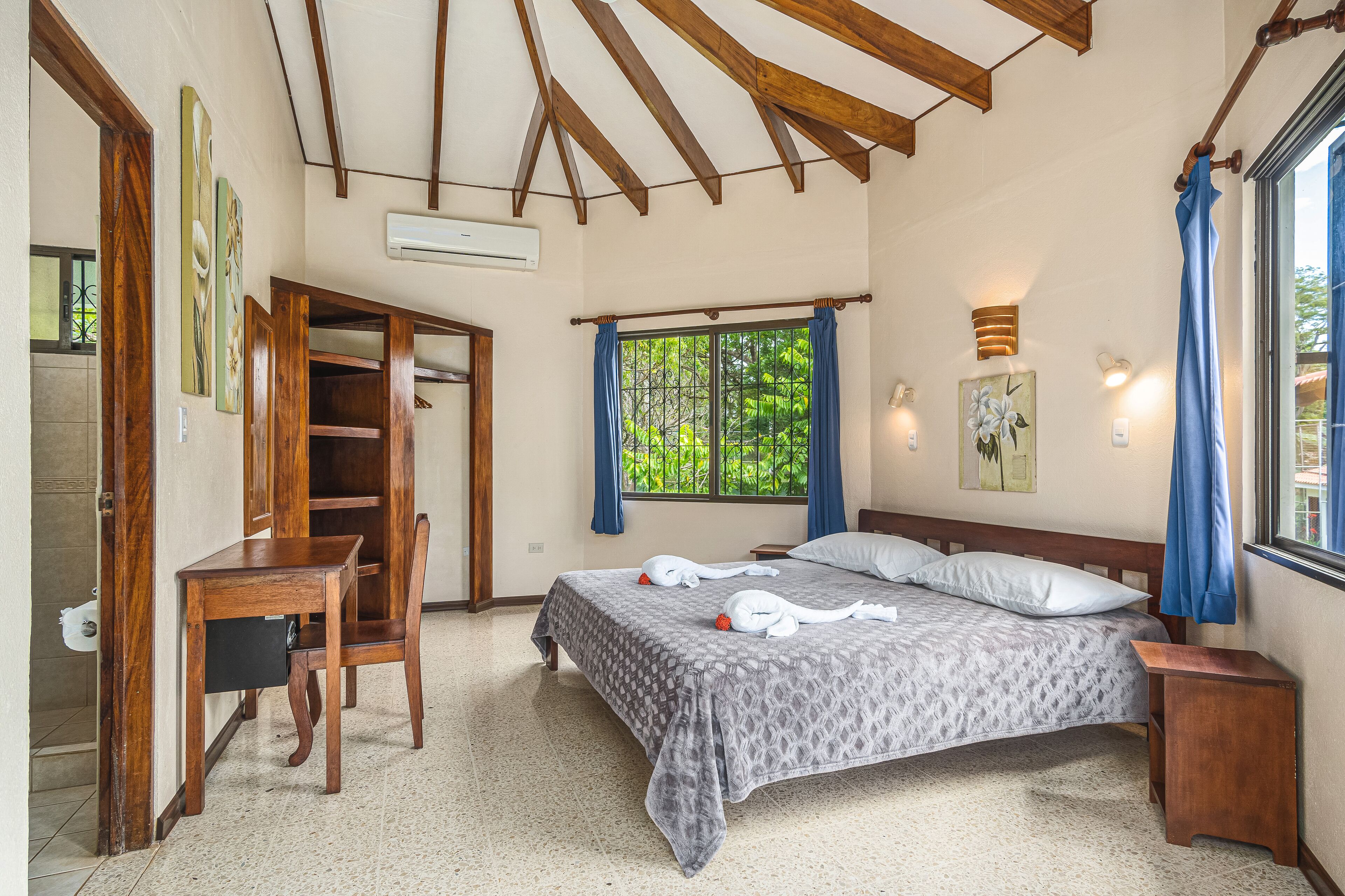 Une chambre à coucher avec un lit, un bureau en bois et une fenêtre avec des rideaux.