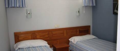 Une chambre à coucher avec deux lits simples, une tête de lit en bois, une petite table de chevet et une fenêtre avec des rideaux.