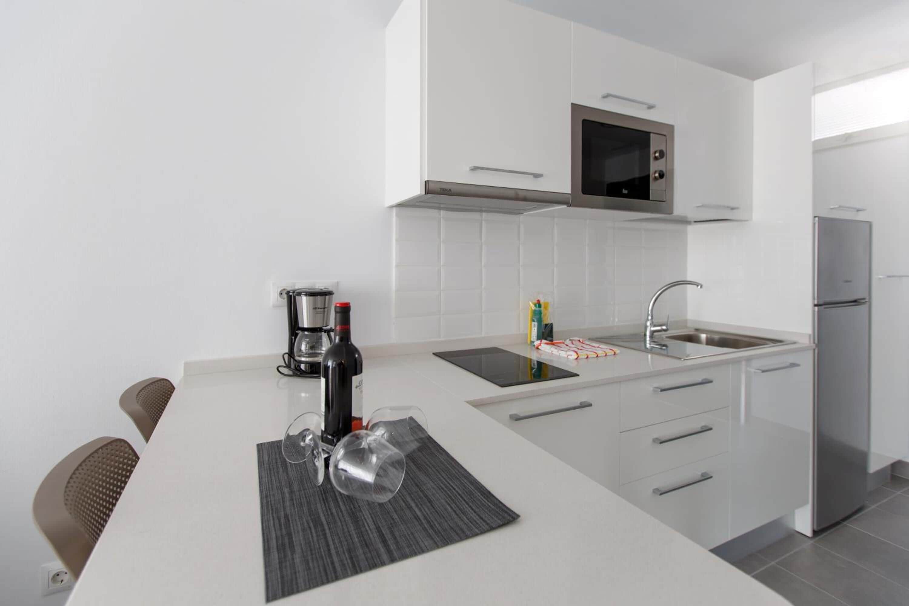 Eine moderne Küche mit weißen Schränken, einer eingebauten Mikrowelle, einem Edelstahlkühlschrank und einer Kaffeemaschine.