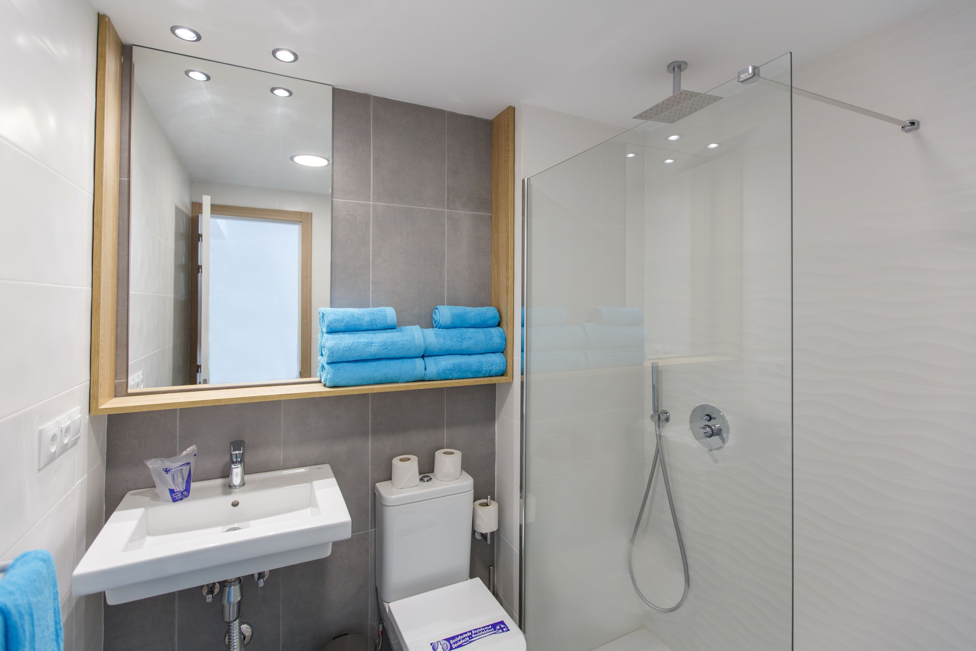 A modern bathroom with a white sink, a toilet, a glass shower enclosure, and a mirror with a wooden frame.
