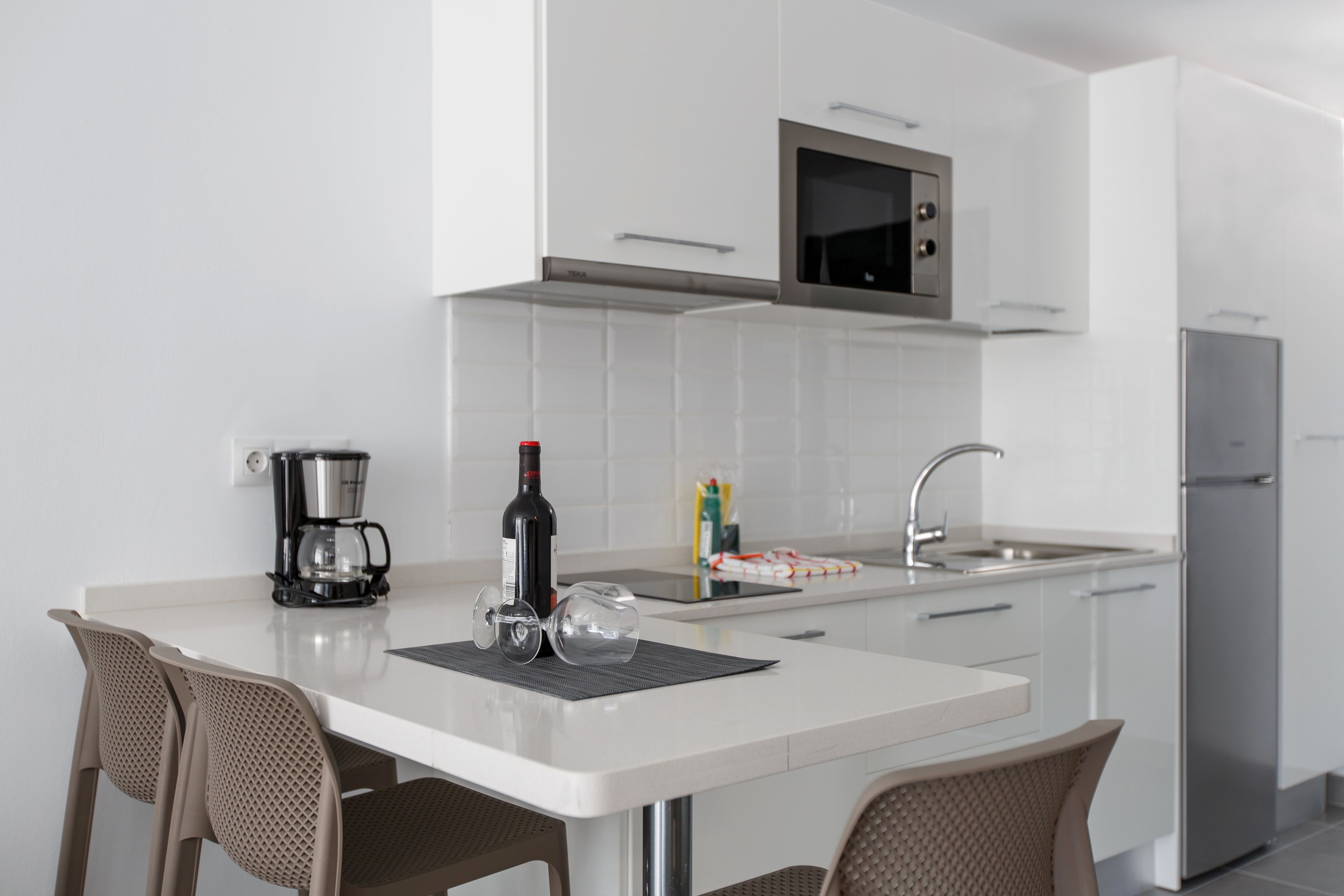 A modern kitchen with white cabinets, a stainless steel refrigerator, a microwave, and a coffee maker on the counter.
