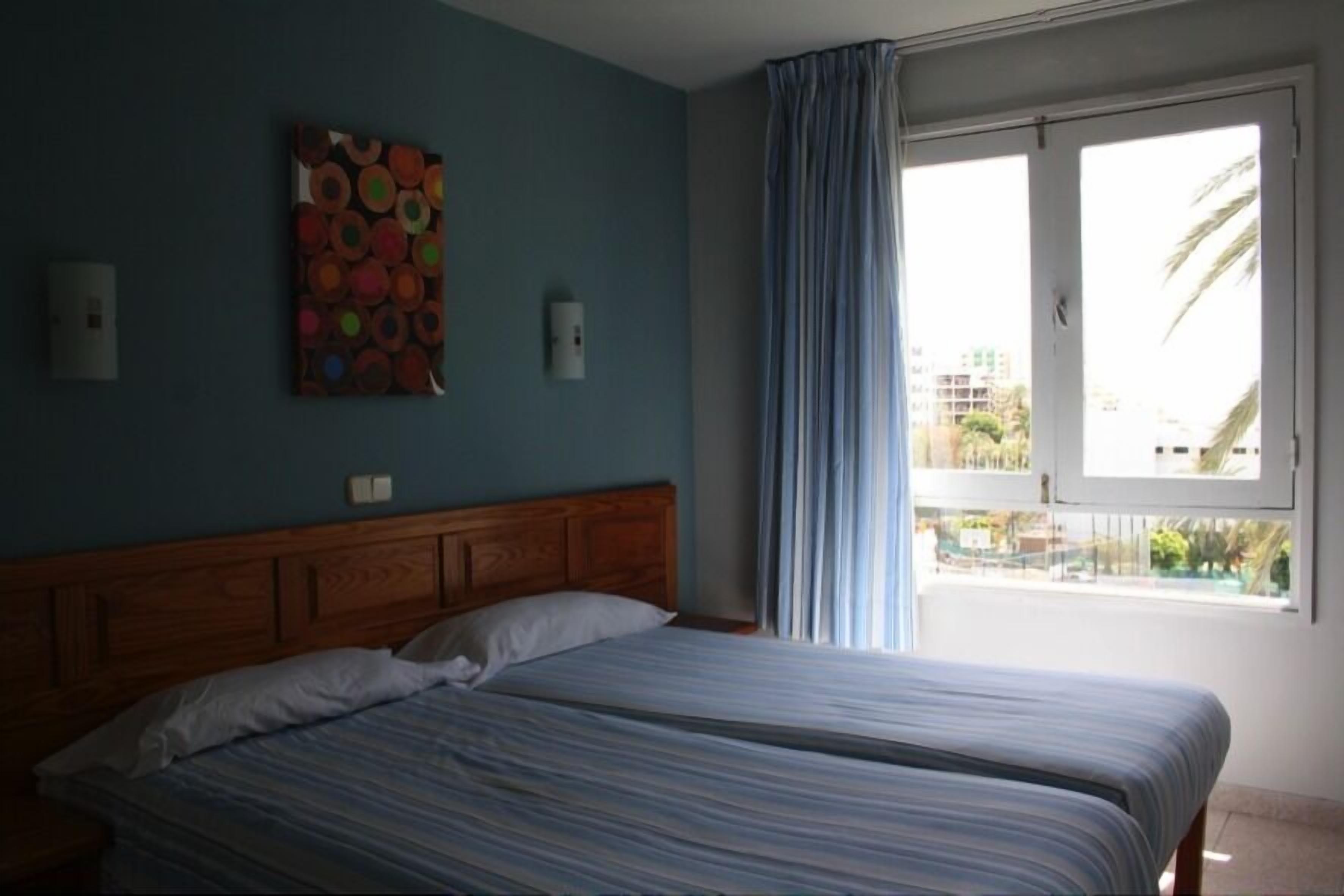 A room with a bed, a wall-mounted artwork, and a window with curtains.
