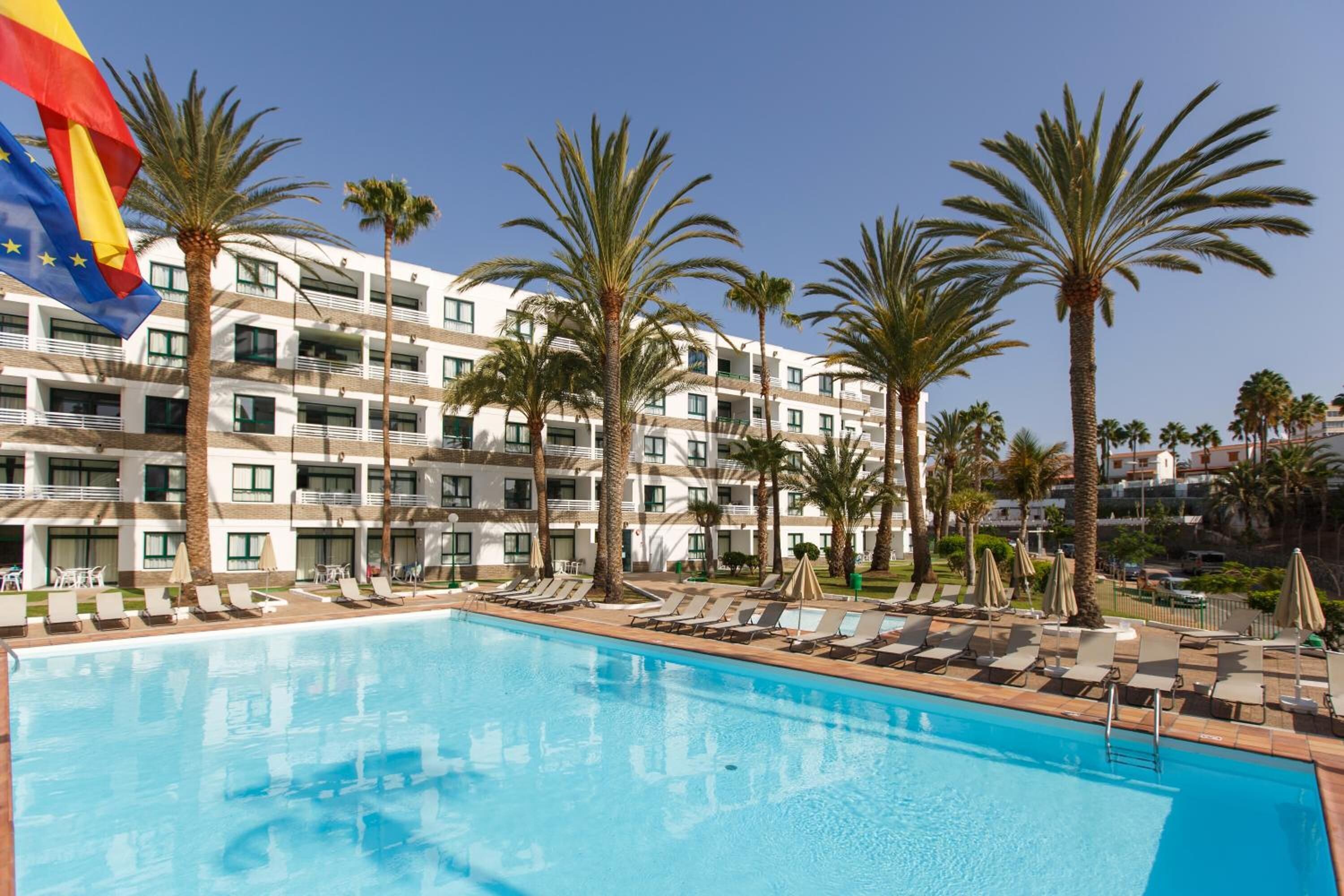 A hotel with a swimming pool, palm trees, and a flag.