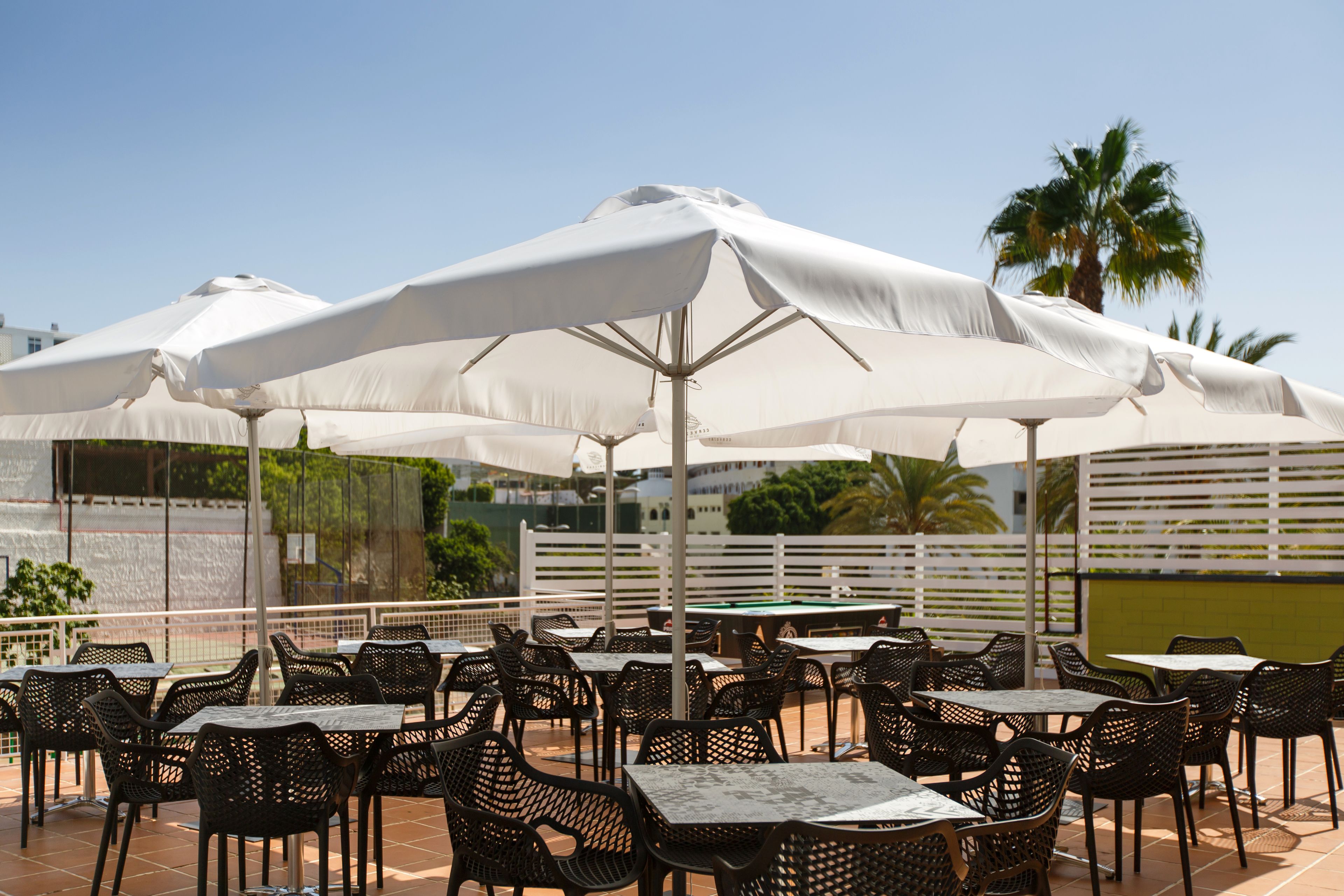 Un patio al aire libre con sombrillas blancas, sillas y mesas negras.