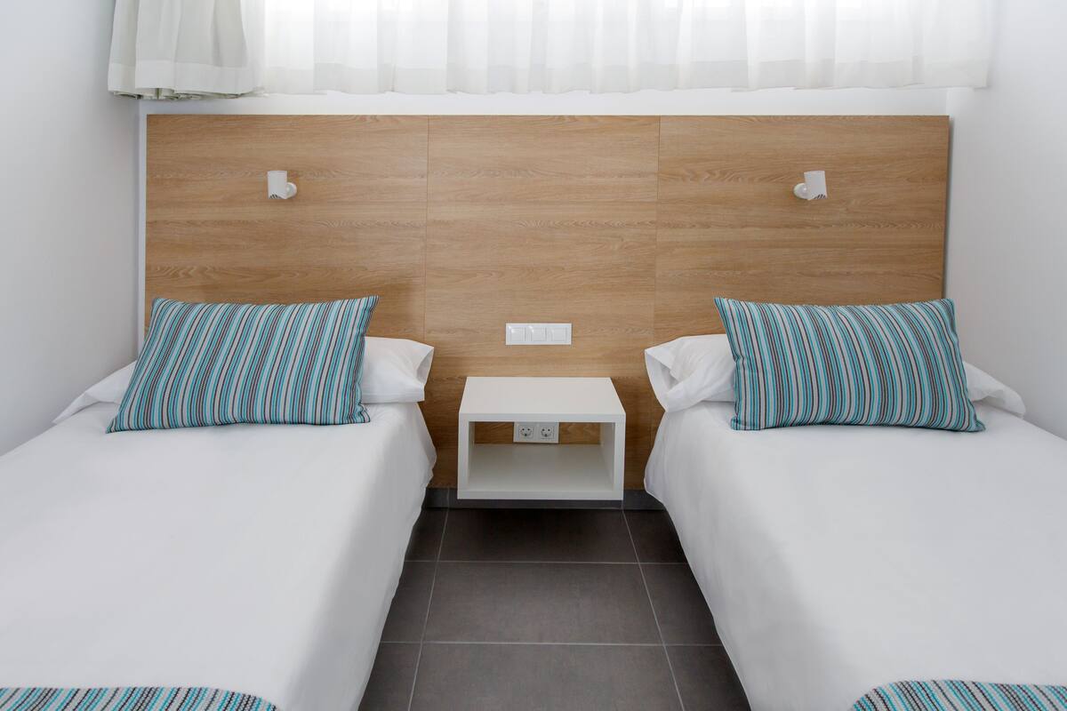 Ein Hotelzimmer mit zwei Einzelbetten, jeweils mit einem gestreiften Kopfkissen und einem weißen Nachttisch.