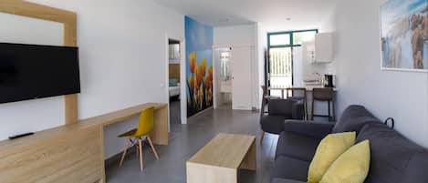 A modern living room with a flat-screen TV, a wooden desk, a grey sofa with yellow cushions, and a painting on the wall.