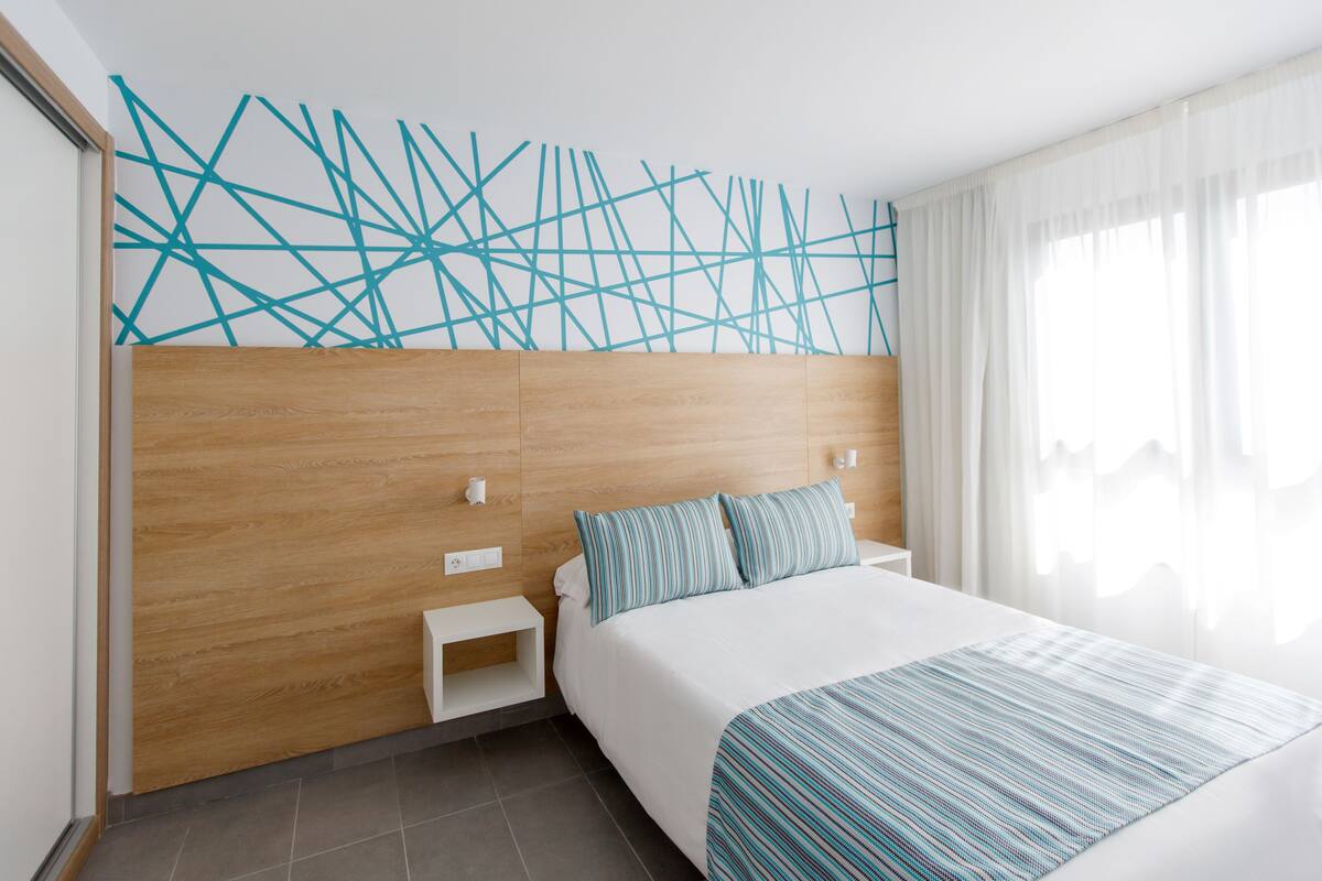 Ein modernes Hotelzimmer mit einem Holzkopfteil, einem großen Bett mit gestreifter Bettwäsche, einem Nachttisch und einem Wandbild.