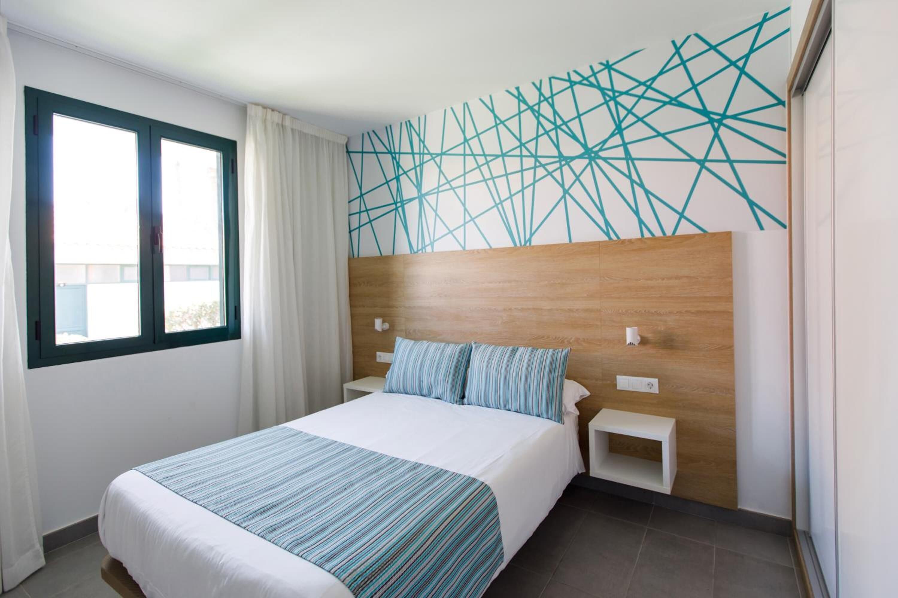 A hotel room with a large bed, a wooden headboard, a nightstand, and a wall with a geometric pattern.