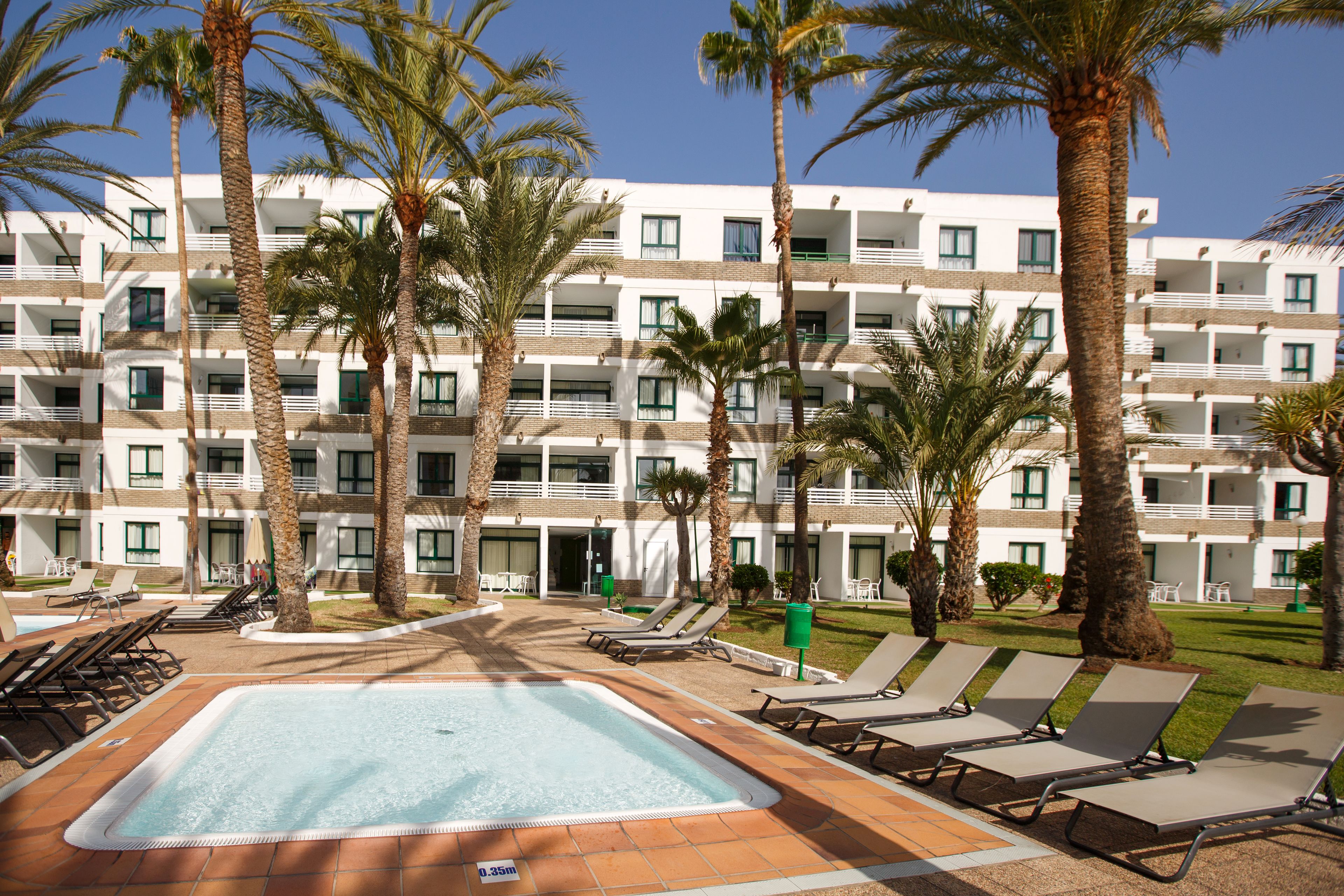 Un hotel con piscina, palmeras y varios balcones.