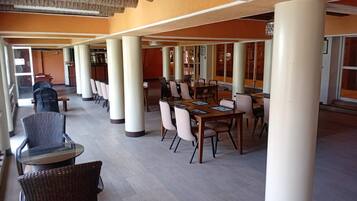 A spacious indoor area with multiple tables and chairs, large pillars, and a view through large windows.
