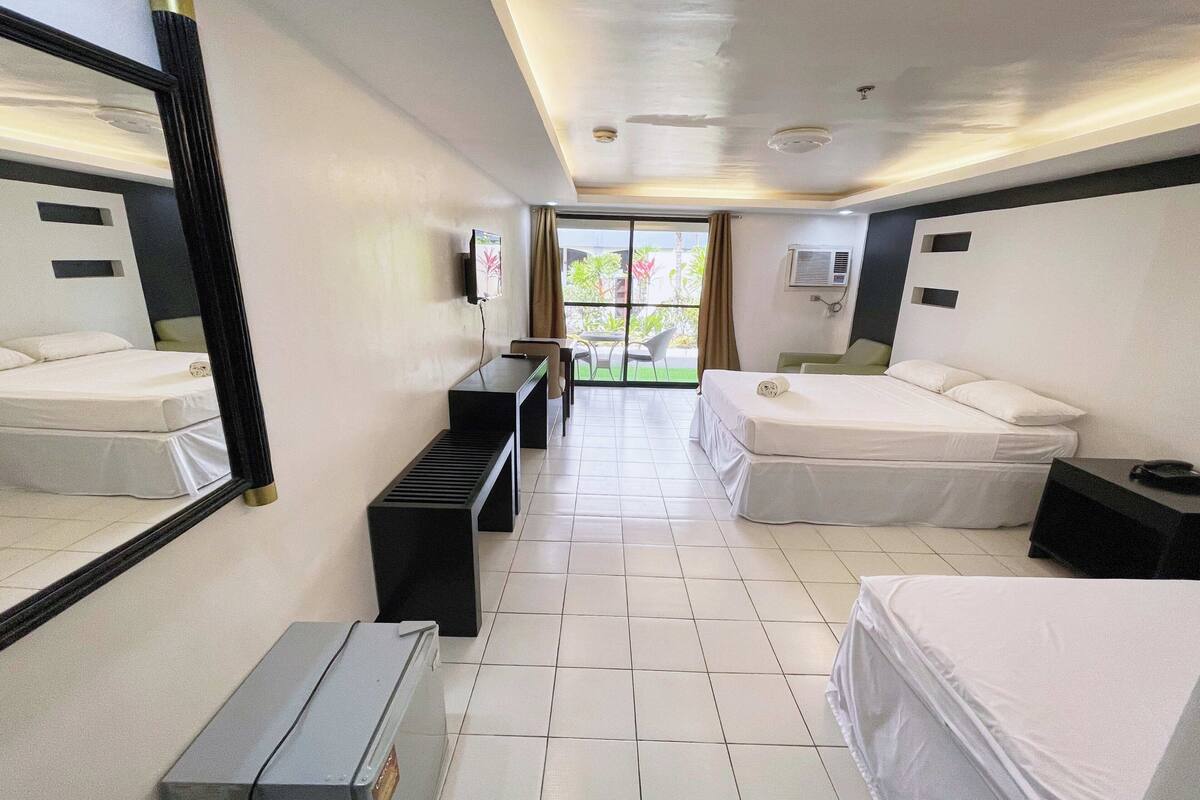 Ein Hotelzimmer mit zwei Betten, einem Schreibtisch, einem Sessel, einem Fernseher und einem Fenster mit Blick auf Grünflächen.