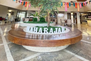 Een lobby met een ronde houten tafel, een centrale boom en de naam 'MAHARAJAD' op de tafel.