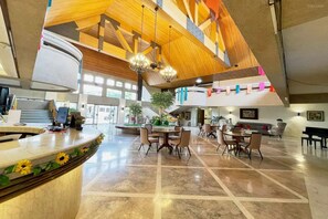 Un vestíbulo amplio con techo alto, una recepción, un comedor con sillas y mesas, y un piano.