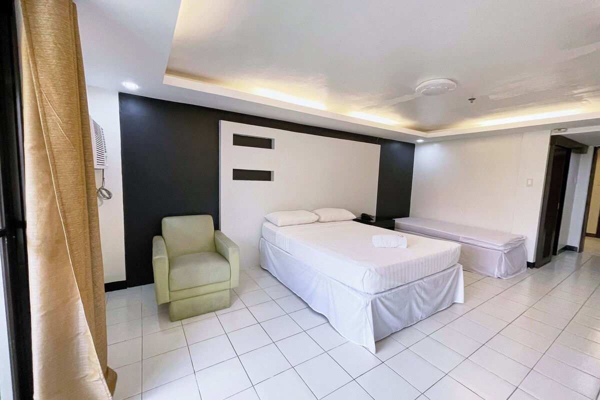 Ein Hotelzimmer mit Bett, Sessel, Bank und Wandklimaanlage.