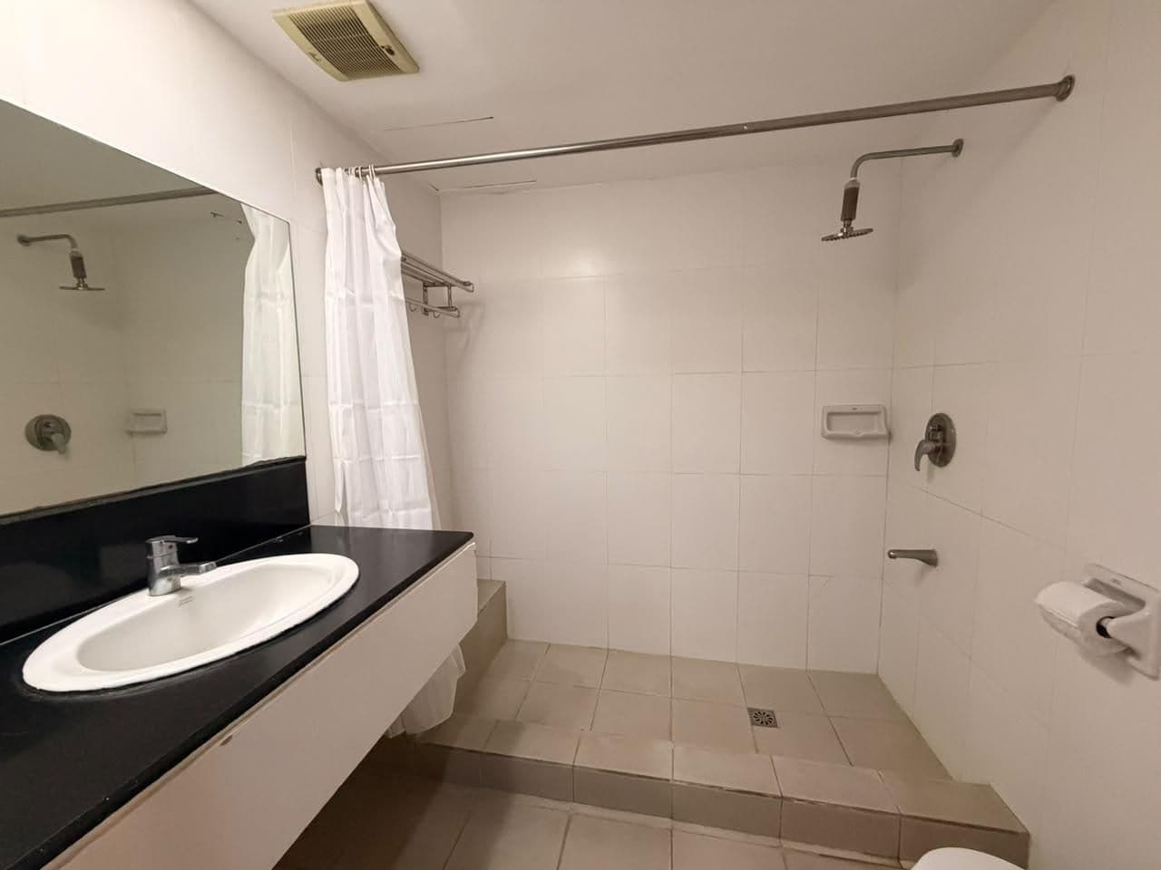 Un baño con lavamanos blanco, espejo, ducha con puerta de cristal y retrete.