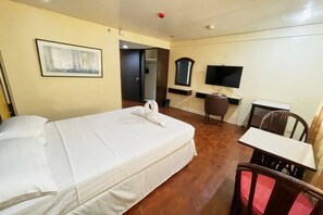 A hotel room with a bed, a desk, a chair, a television, and a framed picture on the wall. - Palette Maharajah Hotel Angeles City (Angeles City)