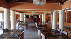Een ruime eetruimte met meerdere tafels en stoelen, een bar in het midden en grote ramen.