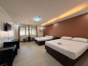 A hotel room with two beds, a desk, a chair, and a TV.