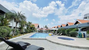 A pool area with lounge chairs, a hot tub, and a building with a red roof. - Maharajah Hotel Angeles City (Angeles City)