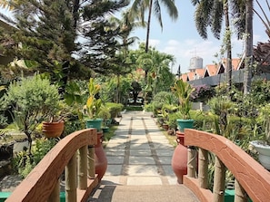A pathway flanked by potted plants and palm trees, leading to a building with a water tank in the background.
