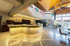 Een hotel lobby met een gebogen receptiebalie, een trap en een zithoek.