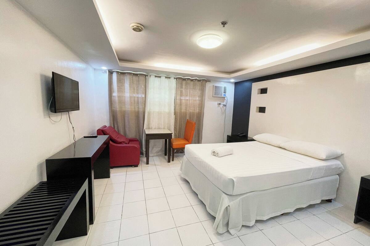 Ein Hotelzimmer mit einem Bett, einem Schreibtisch, einem Stuhl, einem Fernseher und einer Klimaanlage.