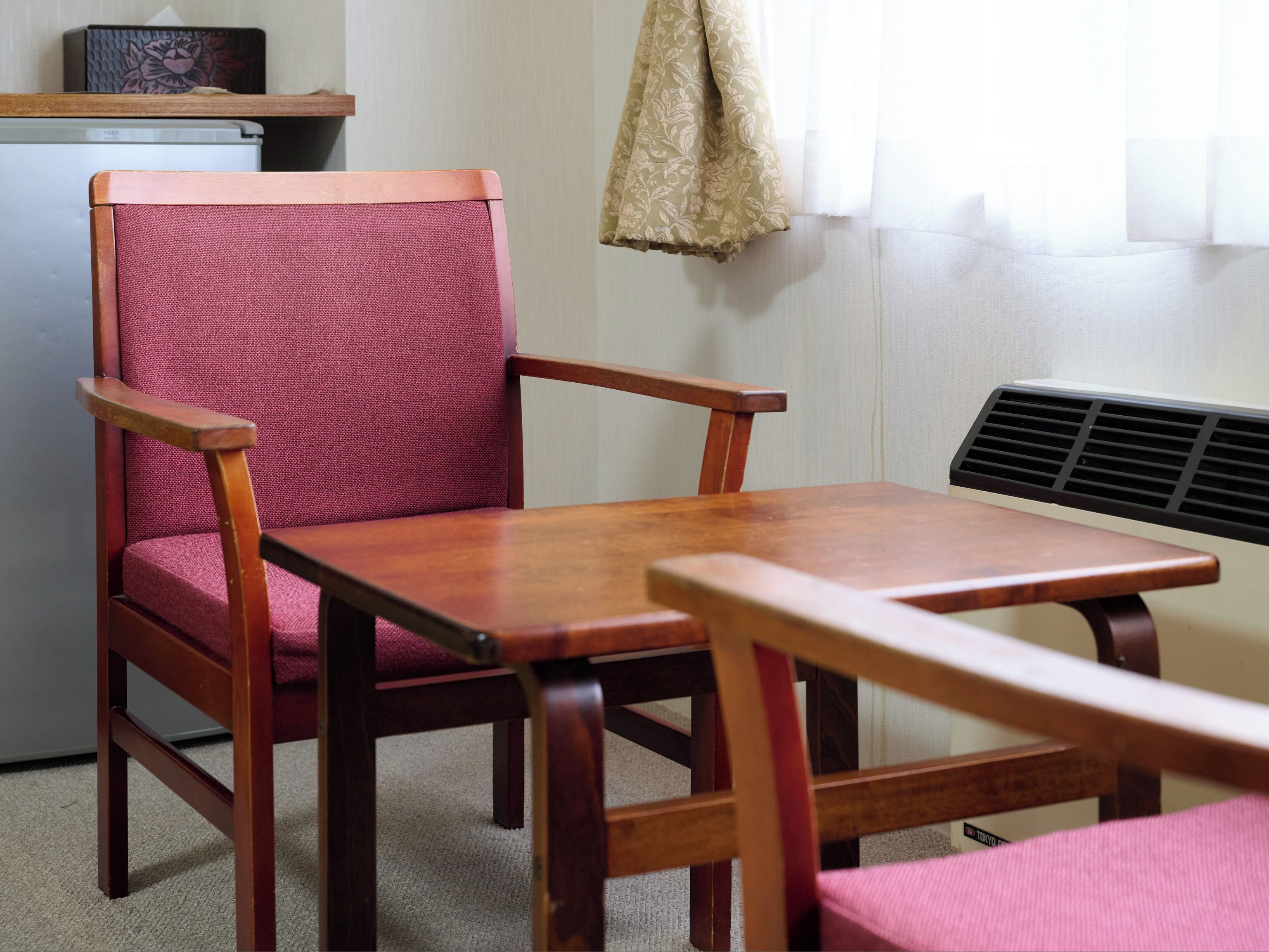 A wooden chair with a cushioned seat and backrest, a small table, and a wall-mounted heater.