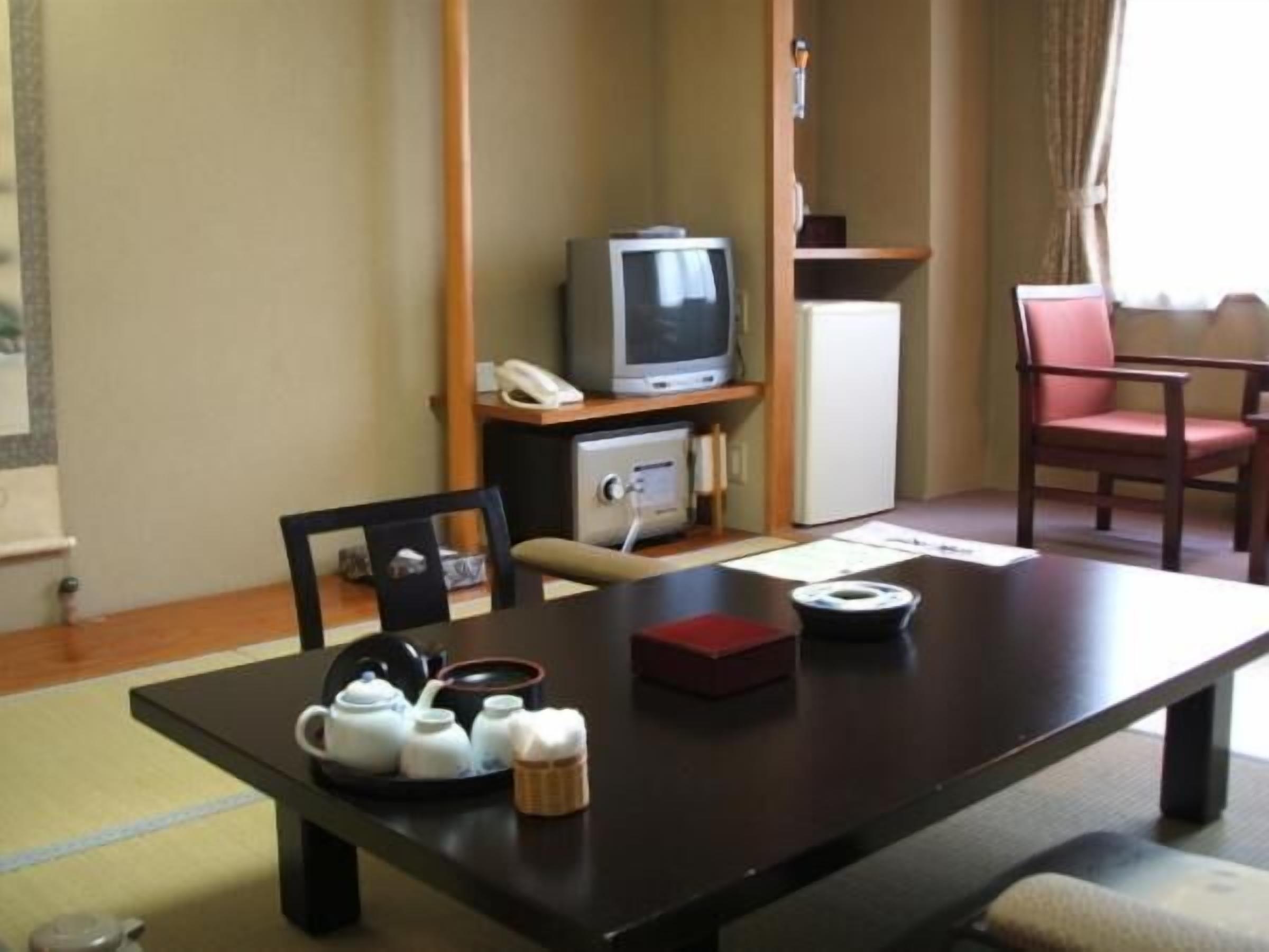 Um quarto com uma mesa de jantar, cadeiras, televisão, frigorífico e telefone.