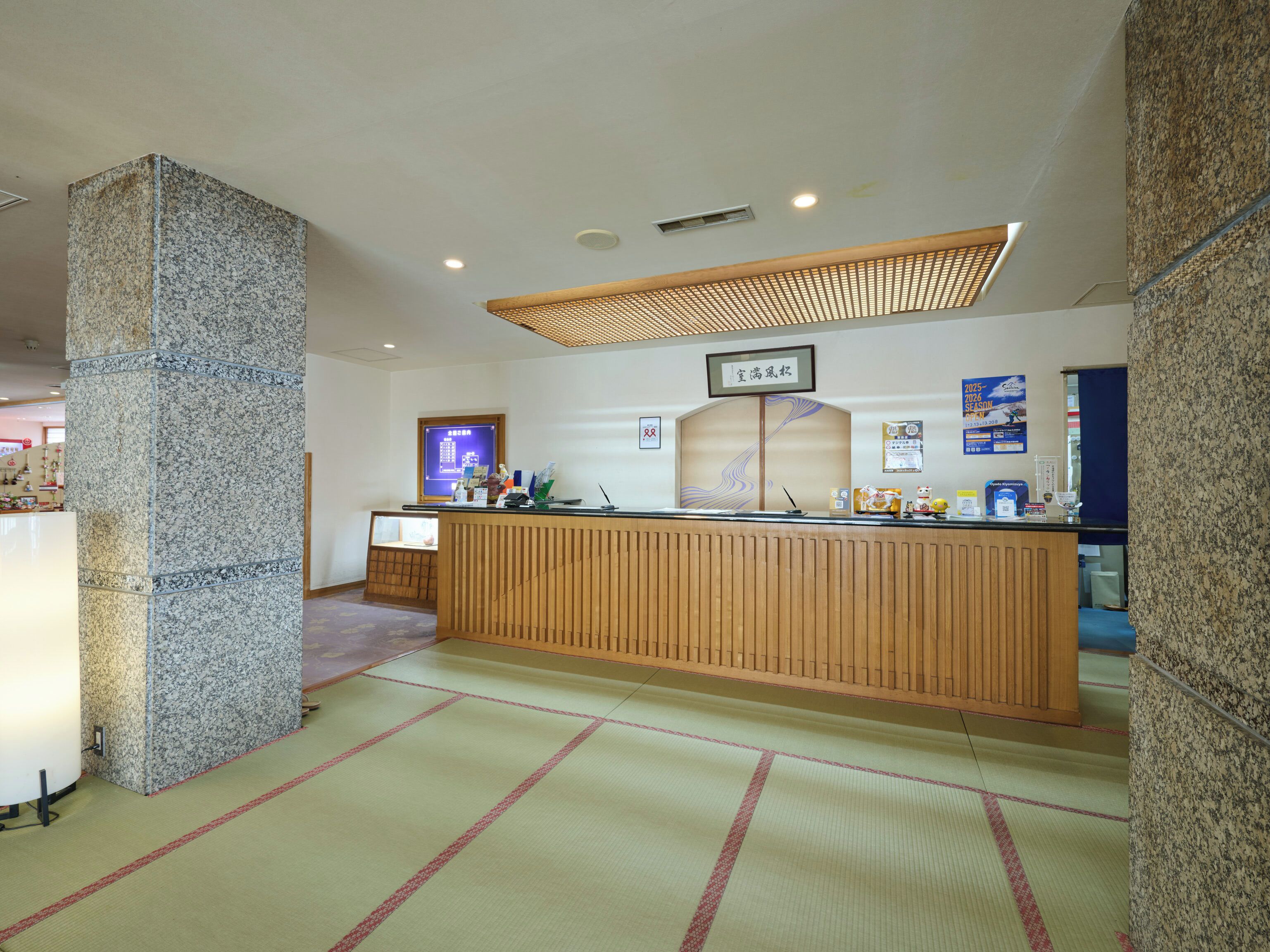 A reception area with a wooden counter, a large pillar, and a traditional tatami mat floor.
