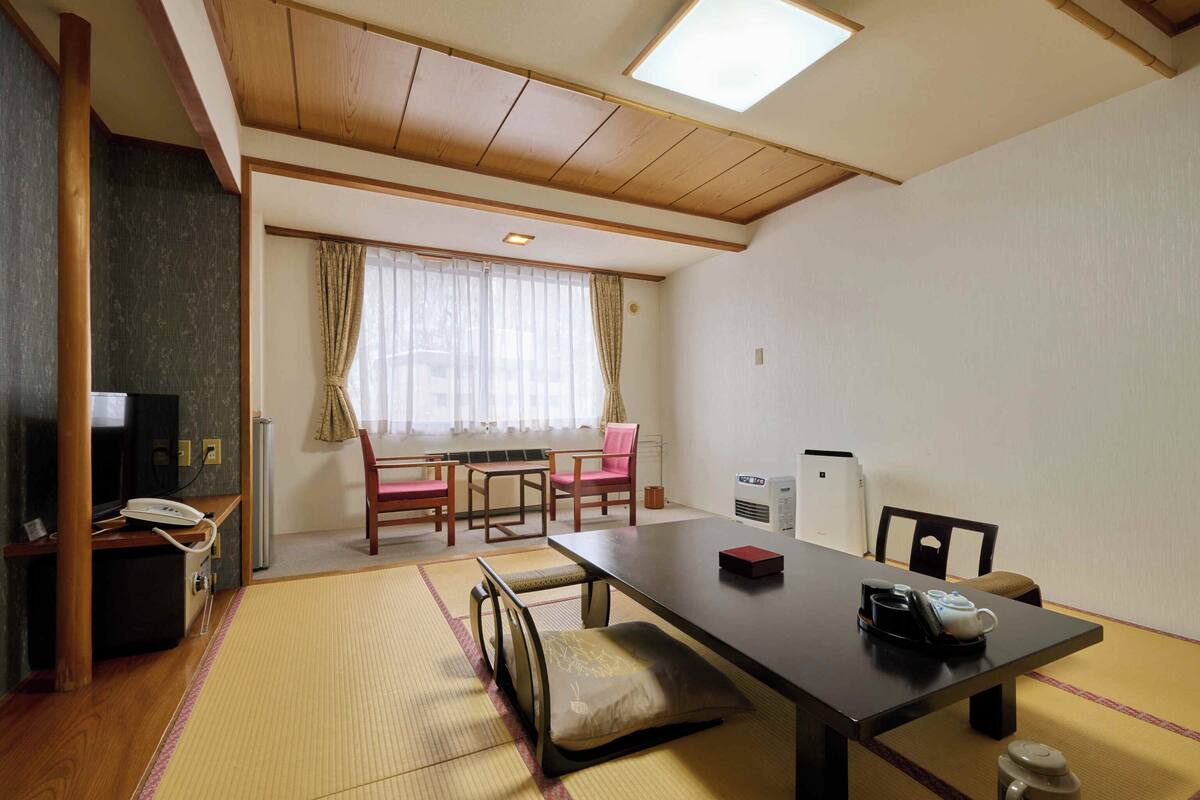 A traditional Japanese room with tatami flooring, a low table, chairs, a television, and an air conditioning unit.