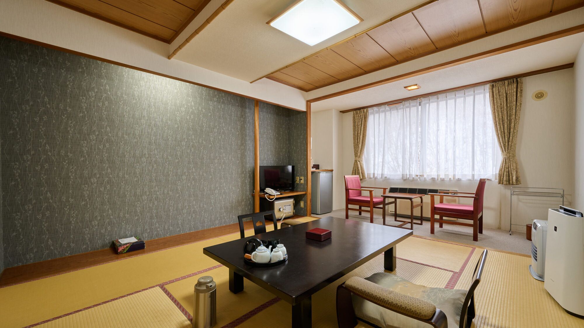 A traditional Japanese room with tatami flooring, a low table, chairs, a television, and a small refrigerator.
