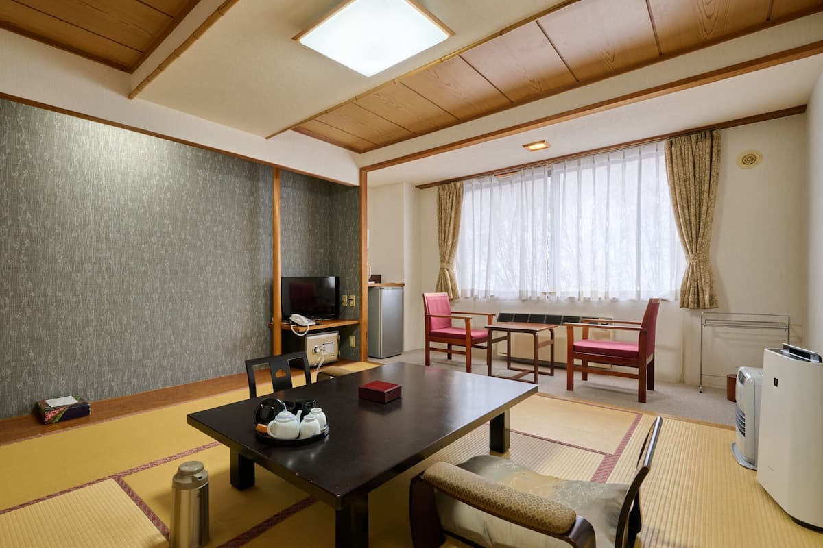 A traditional Japanese room with tatami flooring, a low table, chairs, a television, and a small refrigerator.