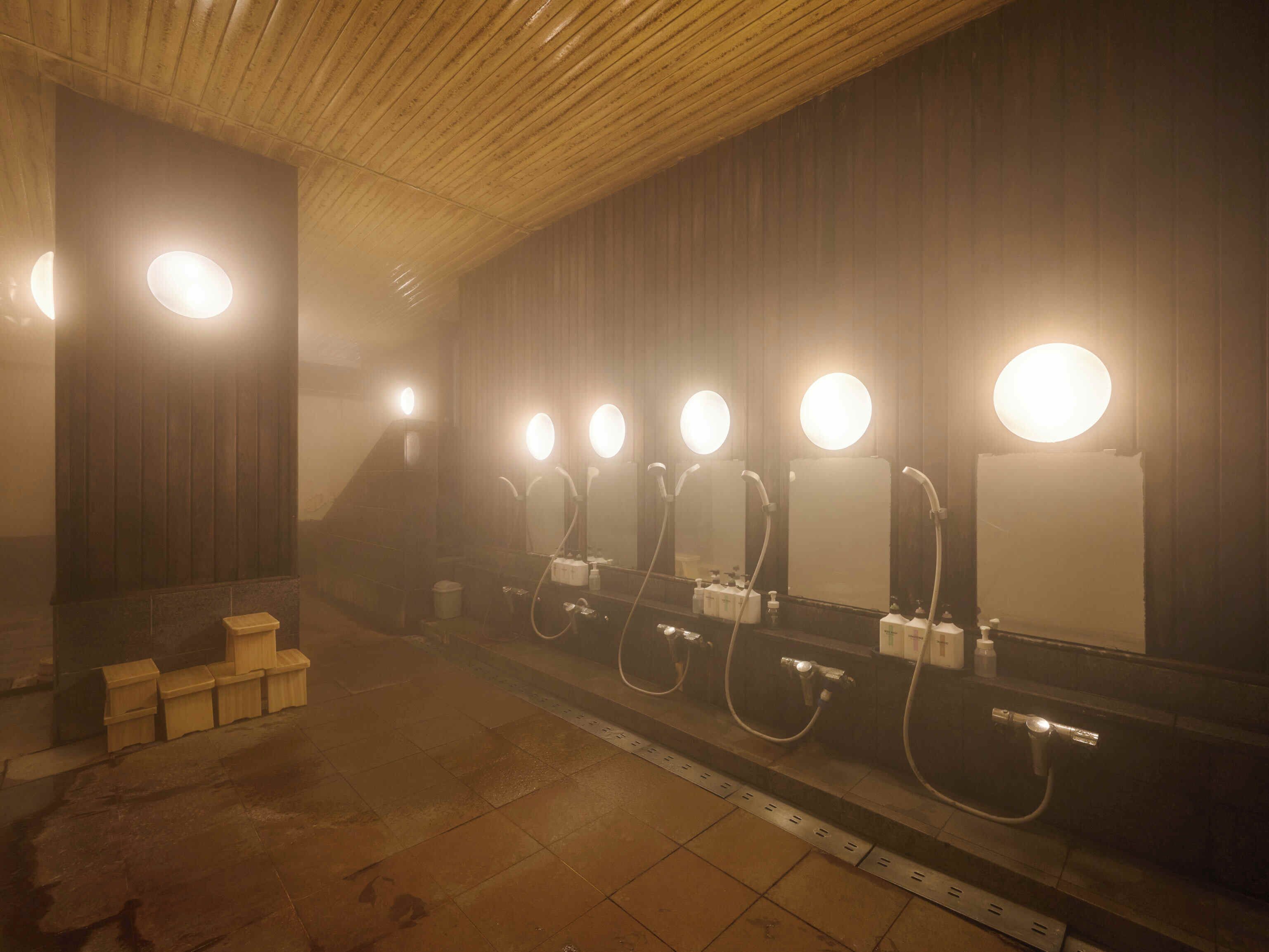 Een badkamer met meerdere wastafels, elk met een ronde spiegel en verlichting erboven.