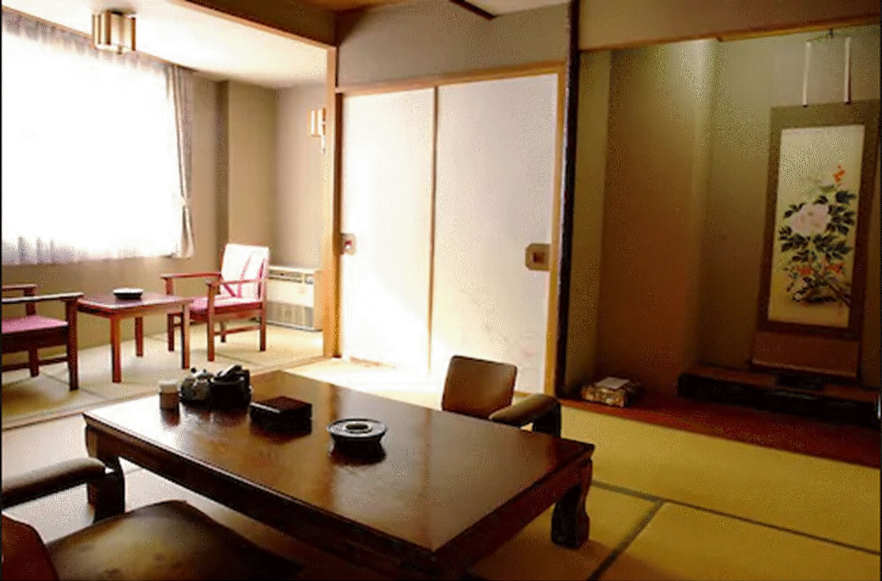 A traditional Japanese room with tatami flooring, a low table with a tea set, a sliding door, and a painting on the wall.