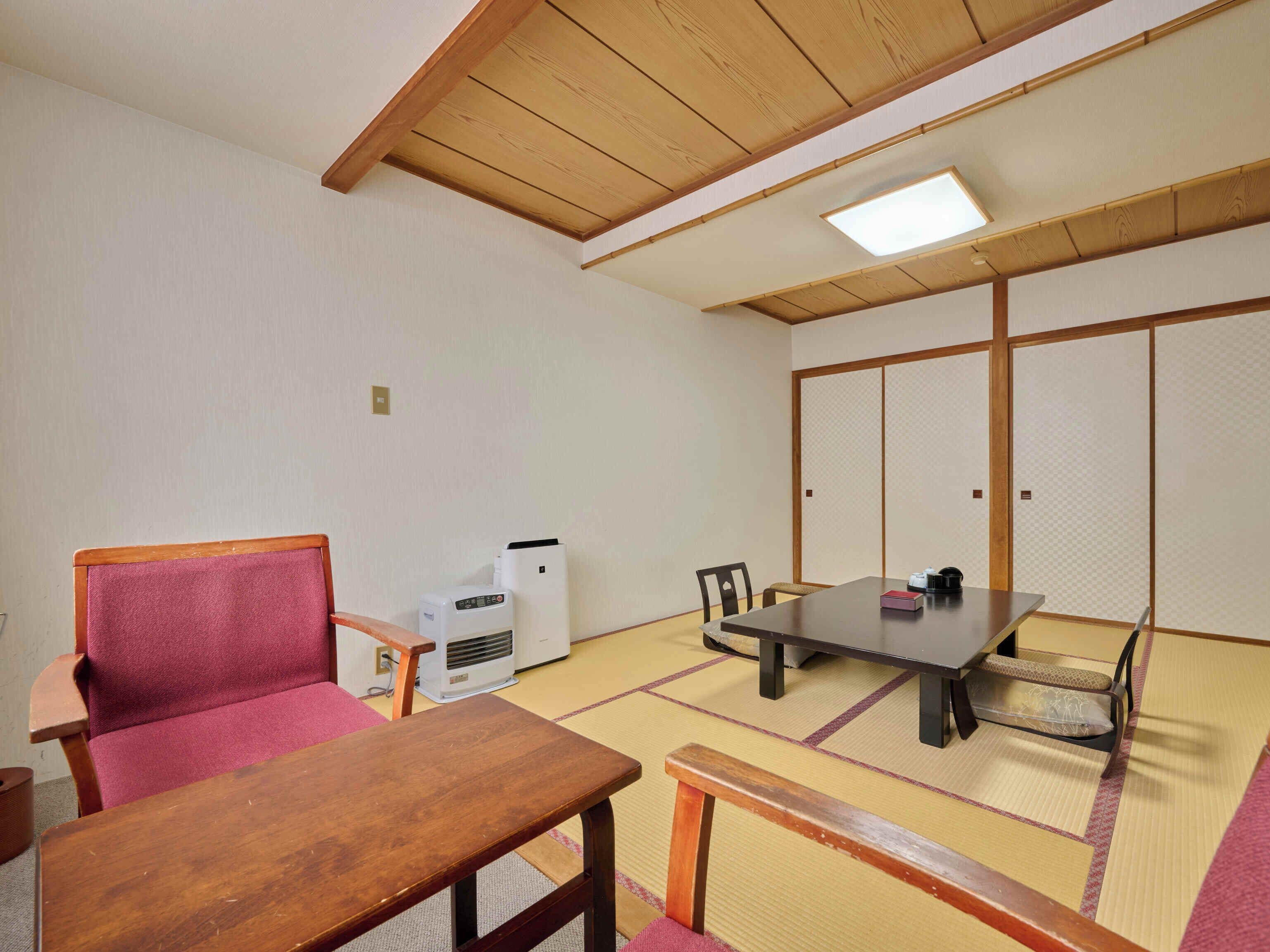A traditional Japanese room with tatami flooring, a low table, a chair, a heater, and a sliding door.